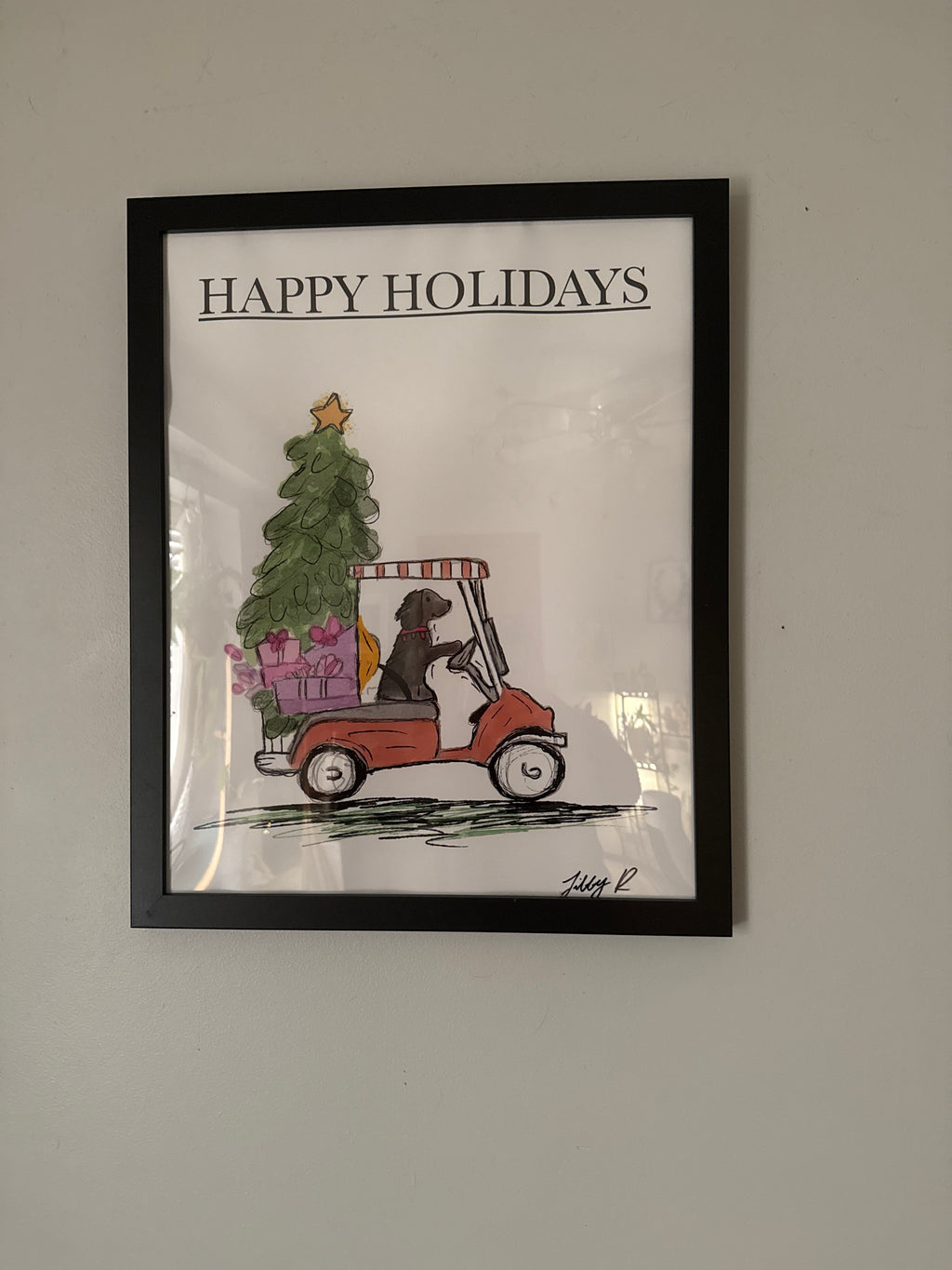 Framed artwork with a Christmas scene and 'Happy Holidays' text on a plain wall.