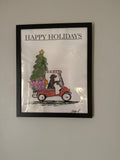 Framed artwork with a Christmas scene and 'Happy Holidays' text on a plain wall.